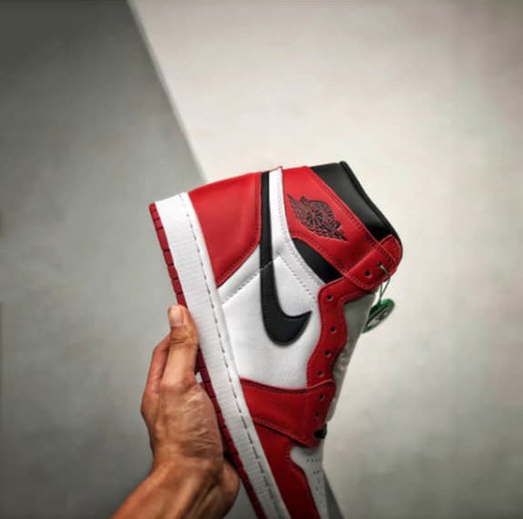 Red and white sneaker held in a hand against a gray background